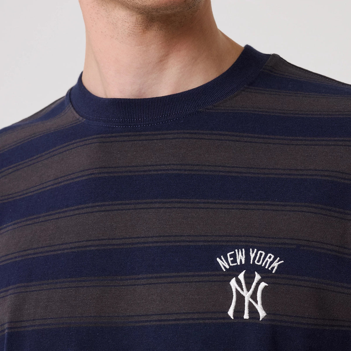New York Yankees MLB Border Navy Oversized T-Shirt, front view showing the navy and dark grey horizontal striped pattern with a raised white New York Yankees logo embroidered on the left chest below the crew neck.