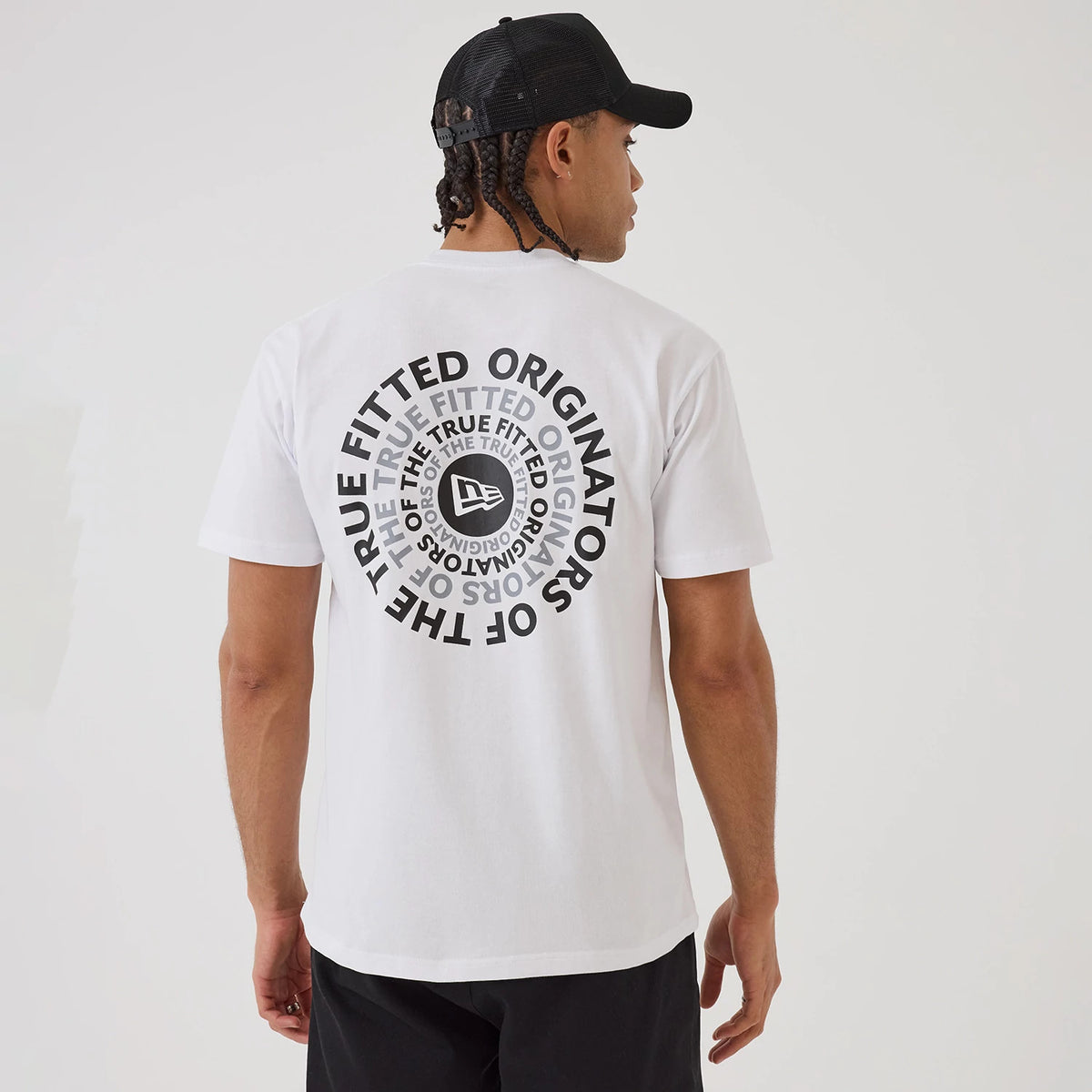 New Era Circle White T-Shirt, rear view showing a prominent circular design in black and grey featuring the words "THE TRUE FITTED ORIGINATORS" and a raised New Era logo at the centre, worn by a model with a black cap.