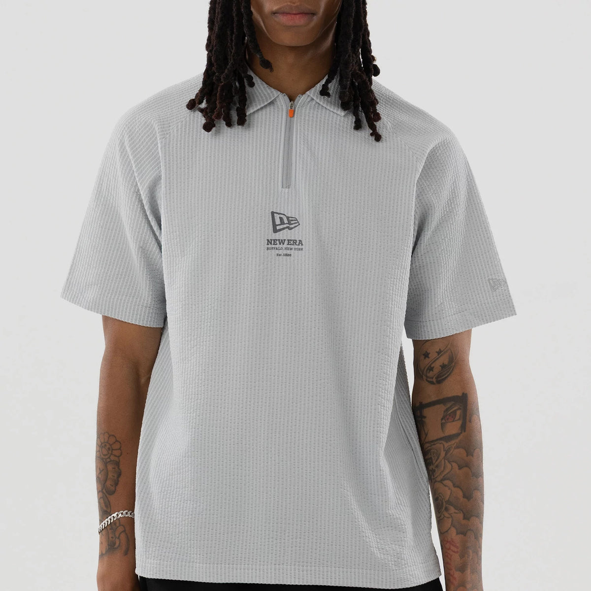 New Era Seersucker Grey Polo T-Shirt, front view showing the light grey textured fabric with a quarter zip and short sleeves, a debossed New Era logo centred on the chest beneath the zip.