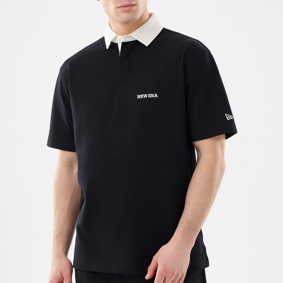 New Era Black Short Sleeve Rugby Shirt, front view on a model featuring a white contrasting collar, embroidered New Era lettering on the chest, and the New Era flag logo on the left sleeve.