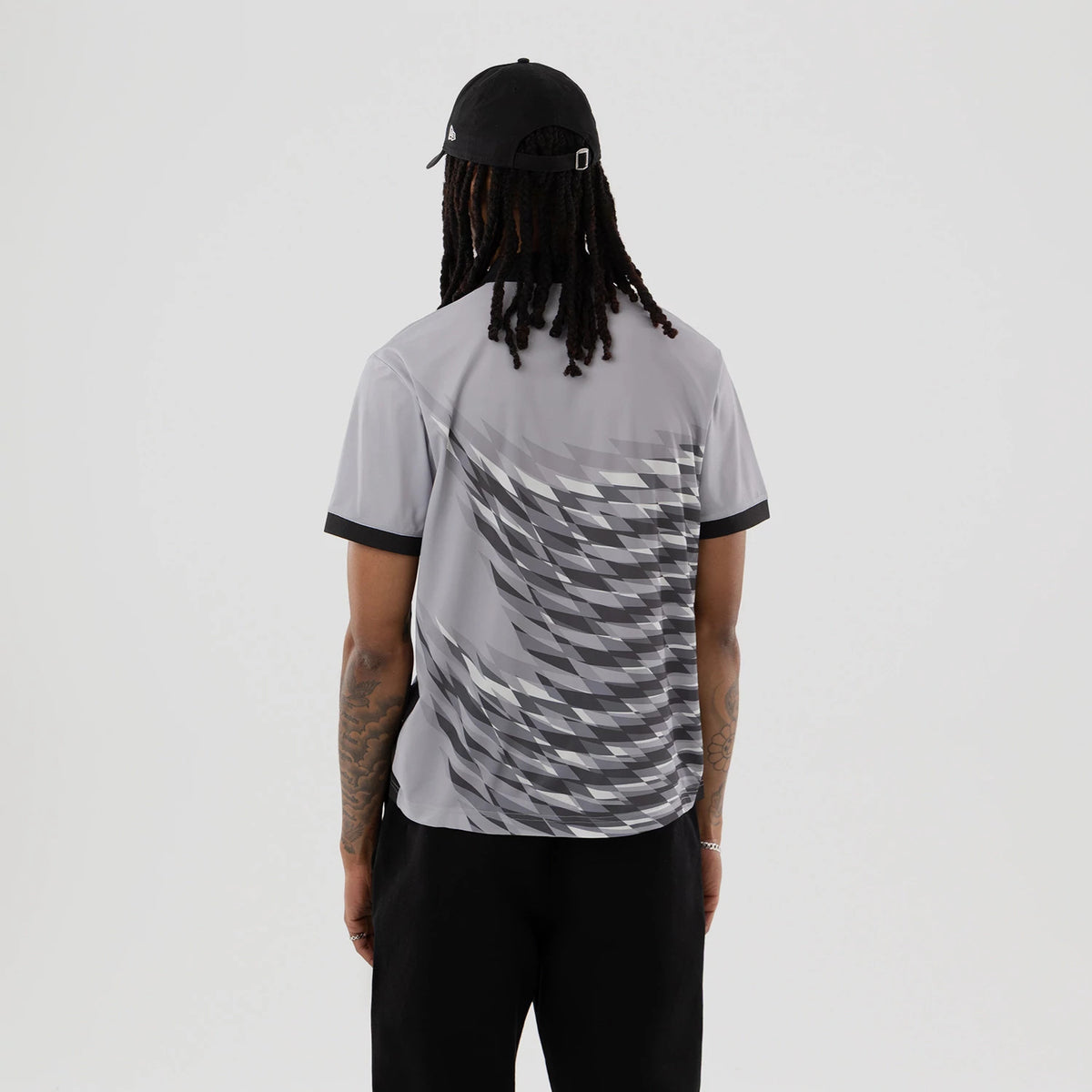 New Era Grid Grey Polo T-Shirt, rear view showing a person wearing the shirt with a geometric pattern in shades of grey across the back, black trim on the sleeves, and a black cap with an embossed logo on the back.