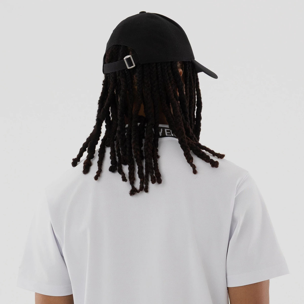New Era Kanoko White Polo T-Shirt, rear view showing the white short-sleeve polo with a black collar featuring the "New Era" text, worn with a black cap with an adjustable strap at the back.