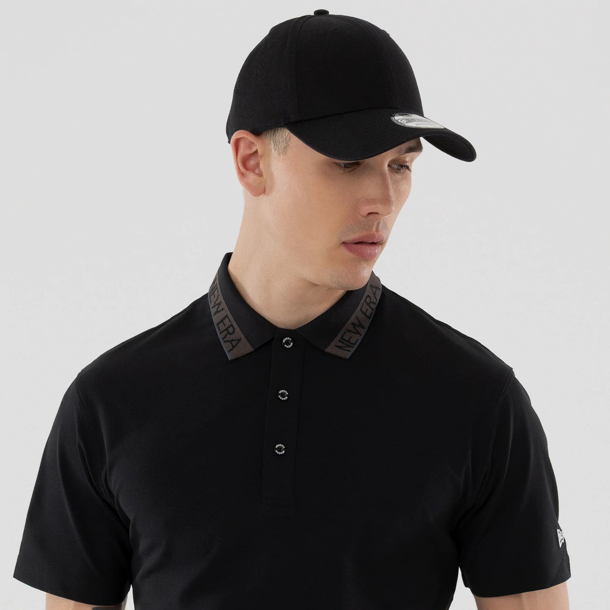 New Era Kanoko Black Polo T-Shirt, front view showing the black polo with New Era branding on the collar, three-button placket in the centre, and short sleeves with a small raised logo on the left sleeve.