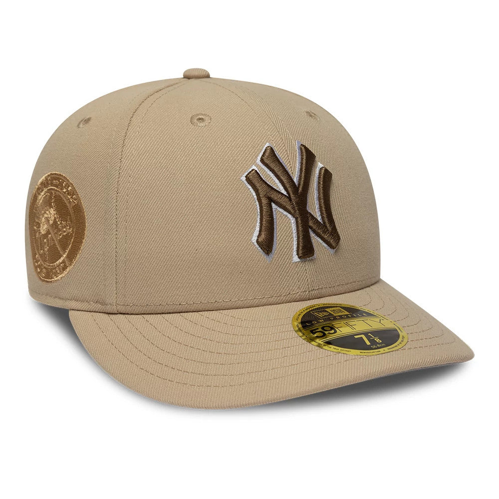 New York Yankees MLB College Varsity Beige Low Profile New Era 59FIFTY Fitted Cap, three-quarter view showing raised brown NY logo embroidered on front panel, gold 59FIFTY size sticker on visor, and brown embroidered circular logo on left side.