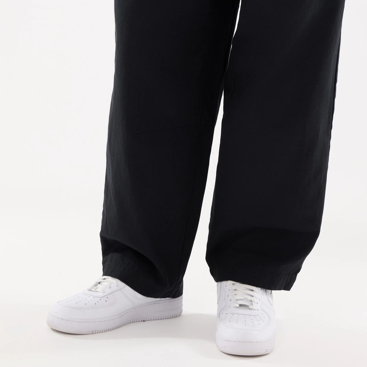 New Era Black Balloon Leg Trousers, front view on a model wearing white trainers, showing the relaxed fit and wide leg silhouette falling loosely over the footwear for a casual look.