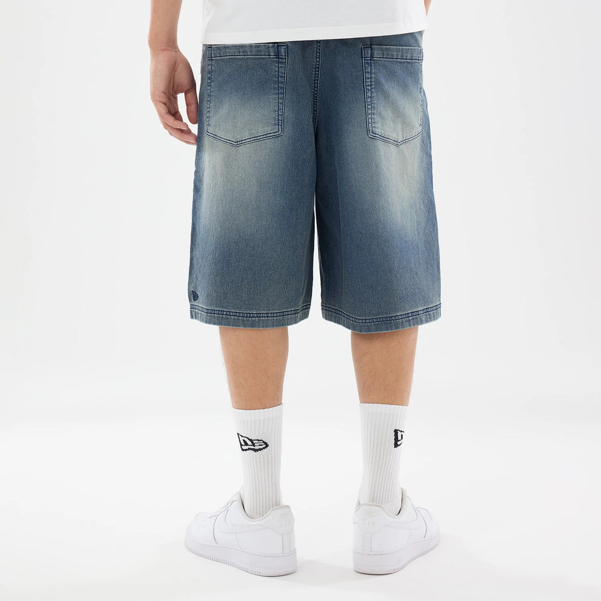 New Era Washed Blue Bermuda Shorts, rear view showing the faded blue denim fabric with two back pockets, hemline reaching just above the knee, and a small debossed New Era logo near the bottom left hem.