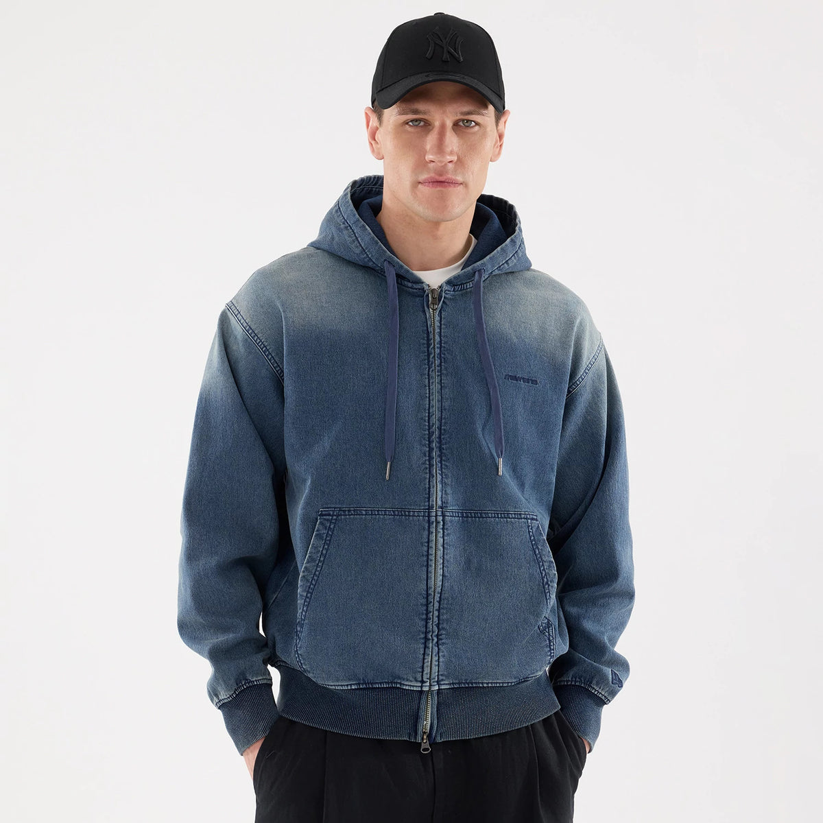 New Era Washed Blue Full Zip Hoodie, on-model view showing the full zip up the front, a drawstring hood, and a raised logo on the left chest, worn by a person also in a black cap with a debossed logo.