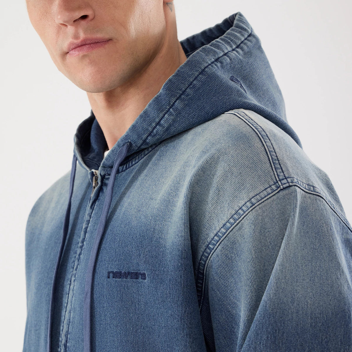 New Era Washed Blue Full Zip Hoodie, three-quarter view showing the blue fabric with a raised New Era logo on the chest, a full-length zip closure in the centre, and hood with eyelets.