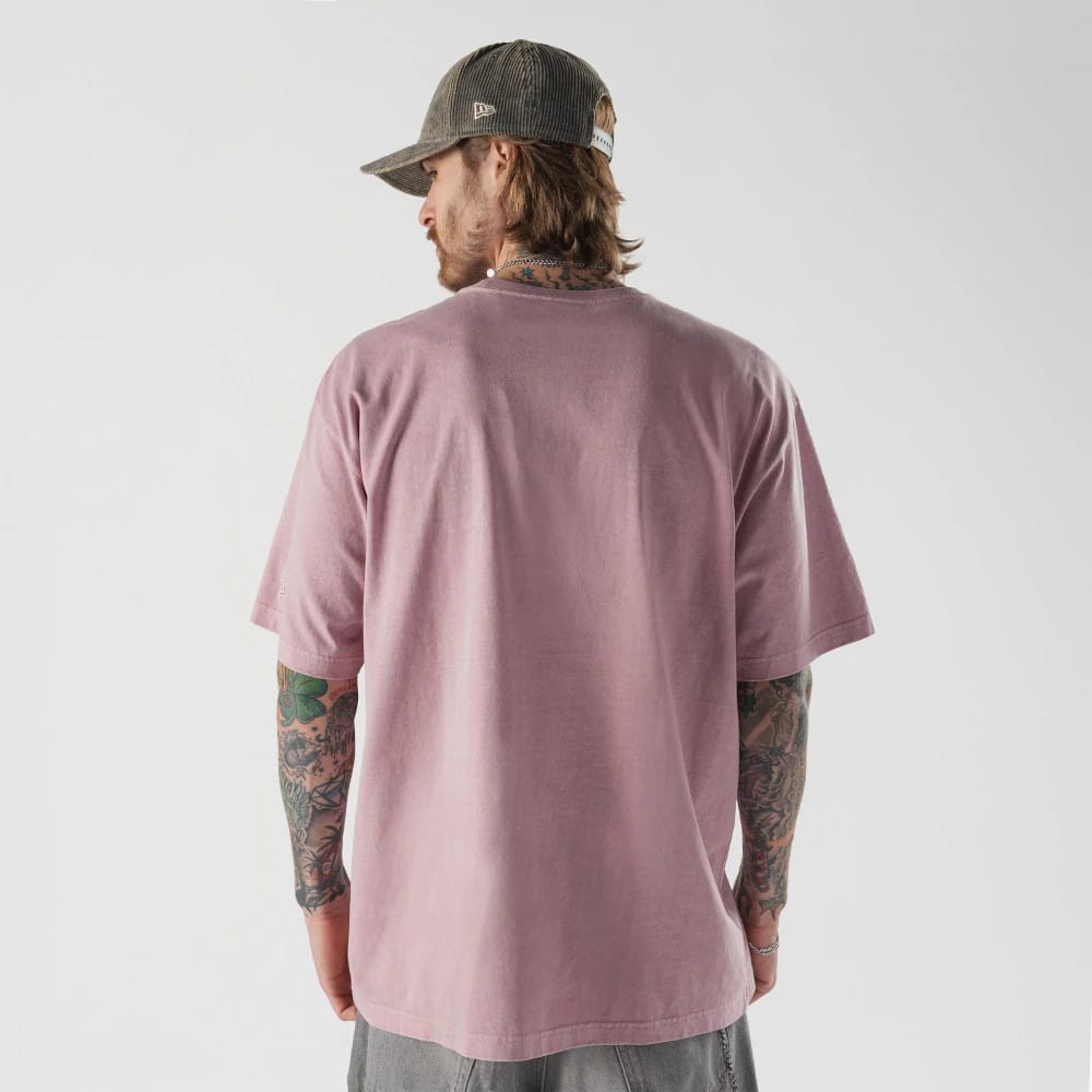 New Era Originators Pink T-Shirt, on-model rear view showing the plain pink fabric with short sleeves, the back of the relaxed fit design and the New Era logo on a grey cap worn by the model.
