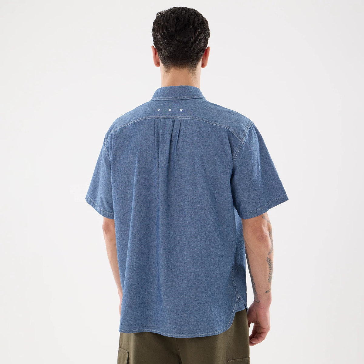 New Era Originators Chambray Dark Blue Short Sleeve Shirt, back view on a model with short sleeves and light stitching, featuring a pleat detail beneath the shoulder yoke and three white buttons on the collar.