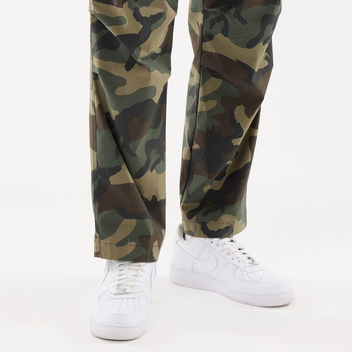 New Era Originators Woodland Camo Cargo Trousers, on-model view showing the full-length loose fit with a classic green and brown camouflage pattern, paired with white sneakers for a casual look.