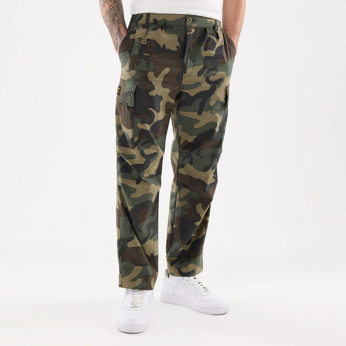 New Era Originators Woodland Camo Cargo Trousers, front view on a model with hands in pockets, highlighting the camouflage pattern, button closures and cargo pocket detail on the leg.