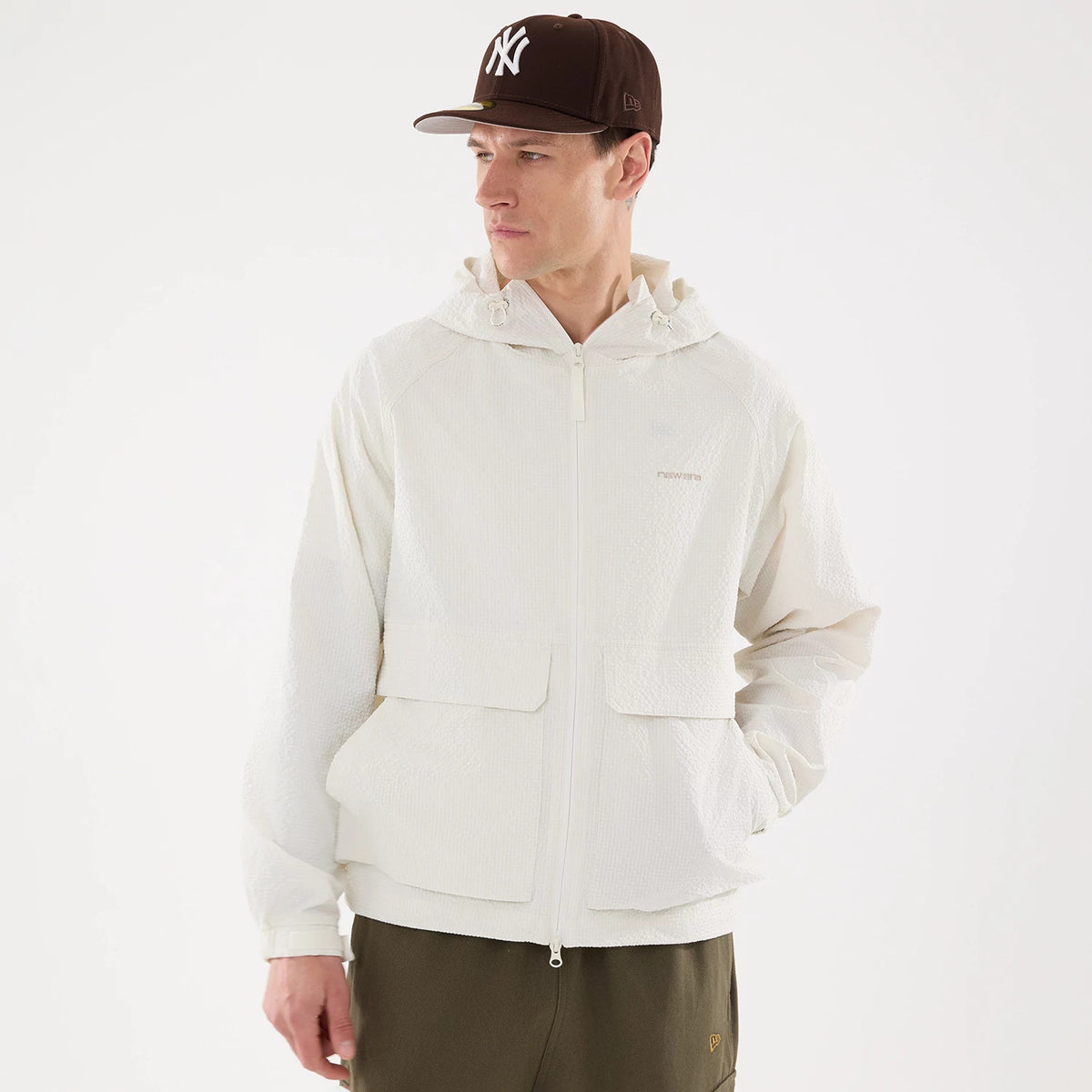New Era Black Label Open White Jacket, on-model view showing a front zip closure, spacious front pockets, and a hood with drawstrings, worn by a person also wearing a brown cap with a white raised logo.