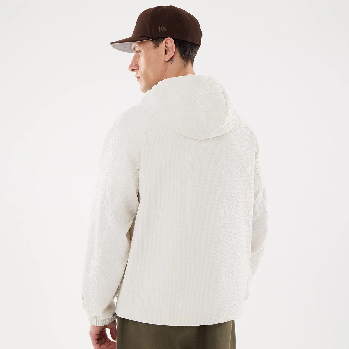 New Era Black Label Open White Jacket, on-model view showing the back of the white jacket with a hood and elastic cuffs, the model is wearing a brown cap with an embossed New Era logo on the side.