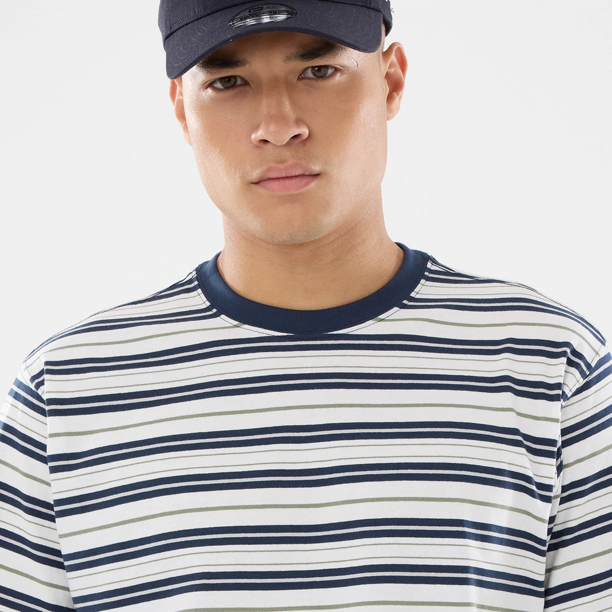 New Era Boarder Stripe White T-Shirt, front view showing horizontal navy and white stripes with a contrasting navy neckline, worn by a person wearing a black cap with a debossed logo on the front.