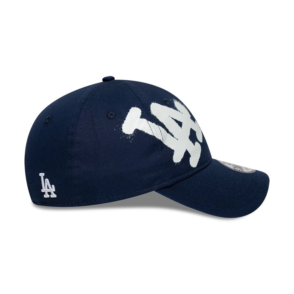 LA Dodgers MLB Spray Paint Dark Blue New Era 9FORTY Adjustable Cap, side view showing the white spray paint-style LA logo on the dark blue crown and the smaller embroidered LA logo on the left side above the curved visor.