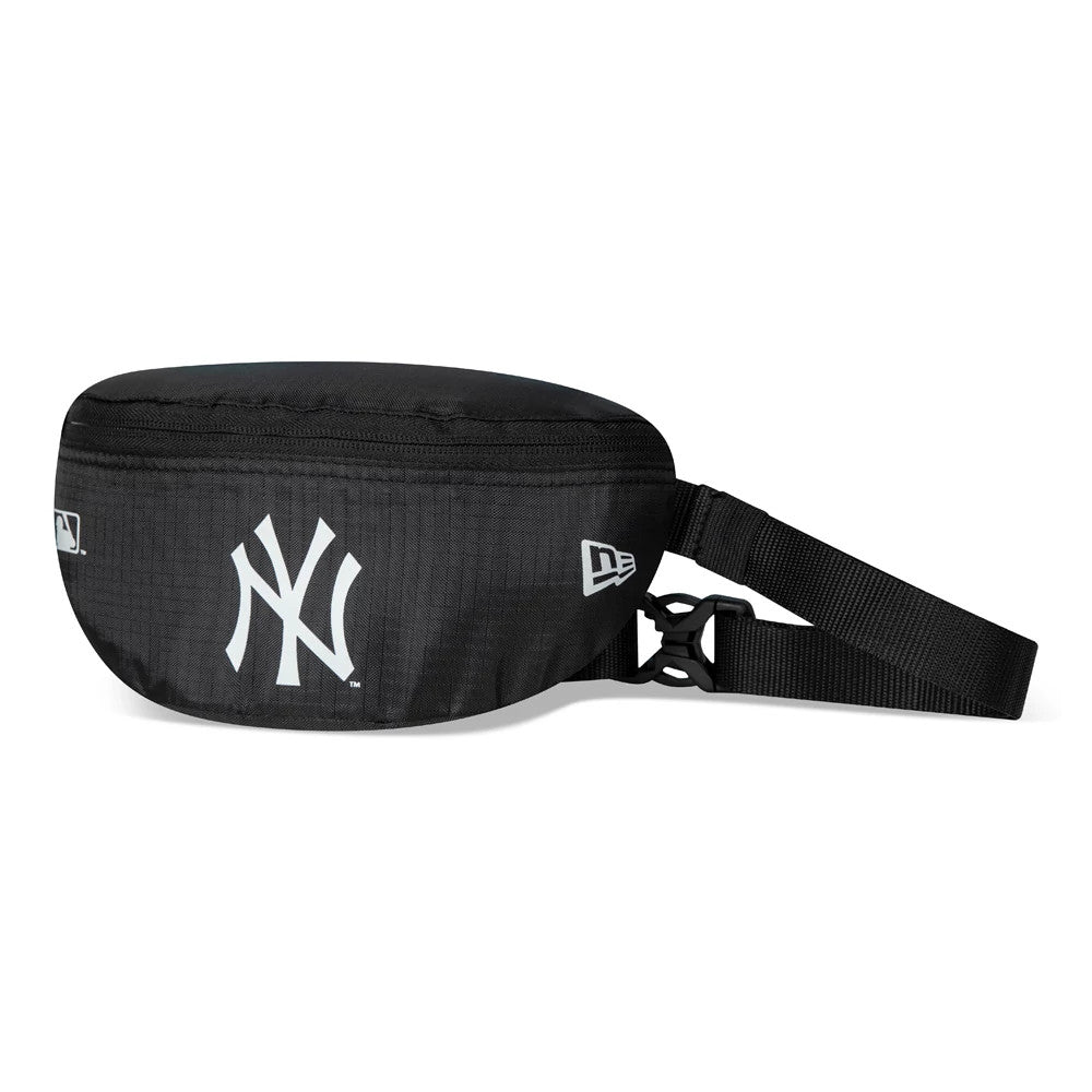 New York Yankees Black Mini Waist Bag, side view showing the sleek black design with a raised New York Yankees logo in white on the front, a zip running along the top and an adjustable black strap with a buckle on the side.