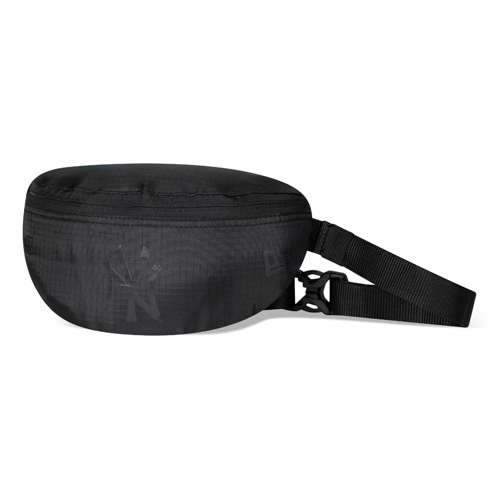 New York Yankees Black On Black Mini Waist Bag, side view showing the compact black shape with a zip closure across the top, a debossed New York Yankees logo on the front, and an adjustable black strap with a buckle attachment.