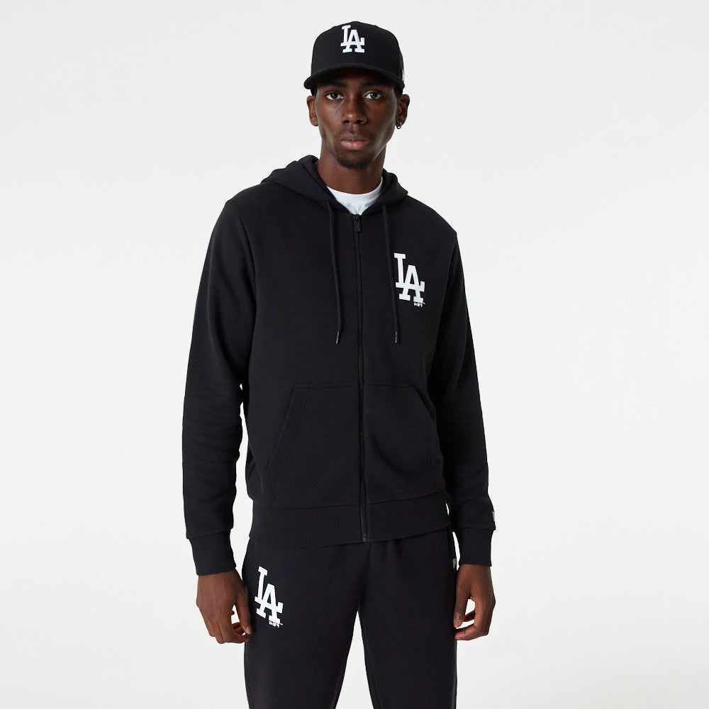 LA Dodgers MLB Essential Black Full Zip Hoodie, on-model view showing a black hoodie with a raised white LA logo on the chest, front zip, drawstrings, and pouch pockets, worn with matching black trousers and a black cap.
