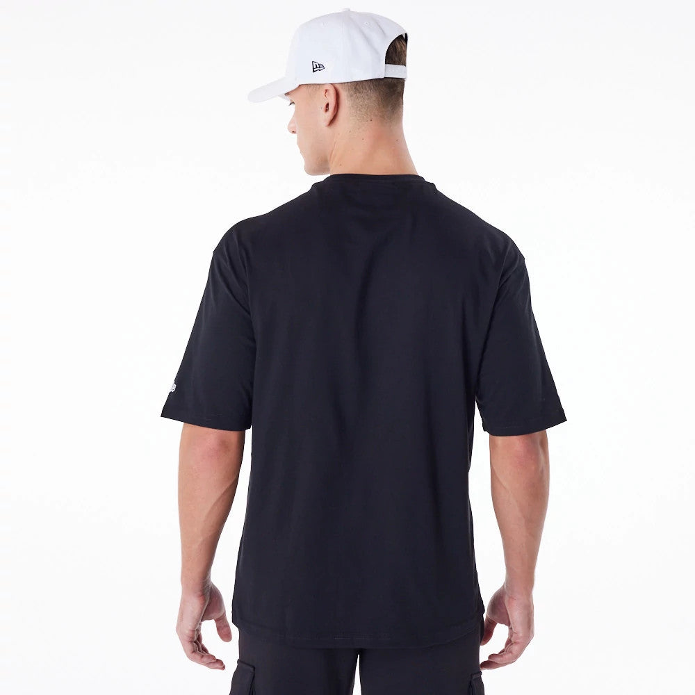 LA Dodgers MLB Essential Black Oversized T-Shirt, on-model rear view showing the solid black back and short sleeves, with a small white debossed New Era logo on a white cap worn by the model.