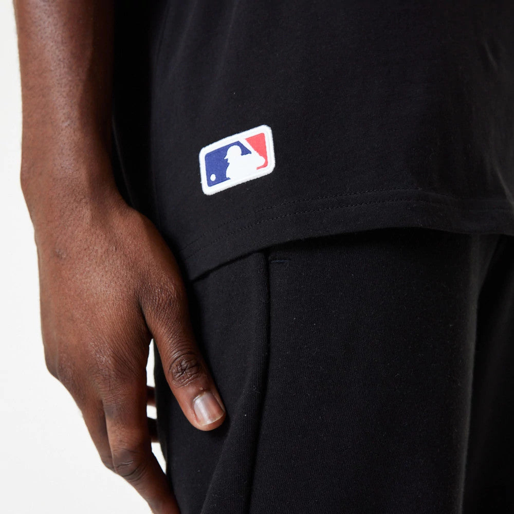 Chicago White Sox MLB Essential Black Oversized T-Shirt, side view showing the small embroidered white and red MLB logo near the hem on the black fabric, with a person's hand resting lightly against the side.