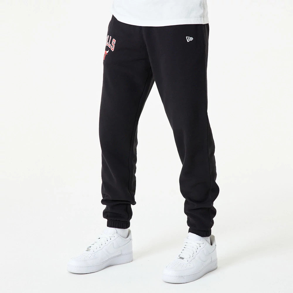 Chicago Bulls NBA Essential Black Joggers, on a model wearing white trainers and a plain white shirt, featuring an embroidered Bulls logo on the upper thigh and a New Era flag logo on the left hip.