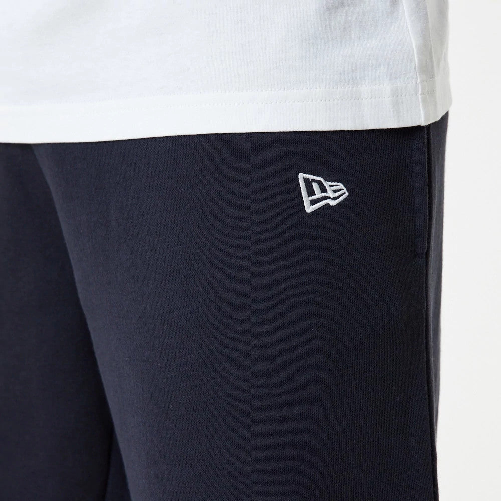 New York Yankees MLB Essential Navy Joggers, close-up showing the white New Era flag logo embroidered on the upper left leg, with a glimpse of a white t-shirt hem above, set against the dark navy fabric.