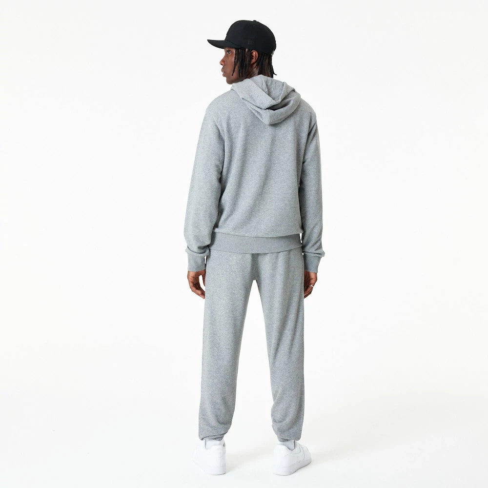New Era Essential Grey Pullover Hoodie, rear view showing the relaxed fit with a drawstring hood, ribbed cuffs, and hem, worn by a person also wearing matching grey pants and a black cap with a debossed logo.