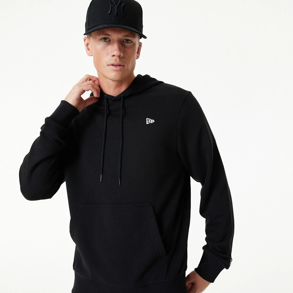 New Era Essential Black Pullover Hoodie, on-model view featuring a black hoodie with a small raised New Era logo on the left chest, long sleeves, ribbed cuffs, and a front pocket, paired with a black cap displaying a raised logo.