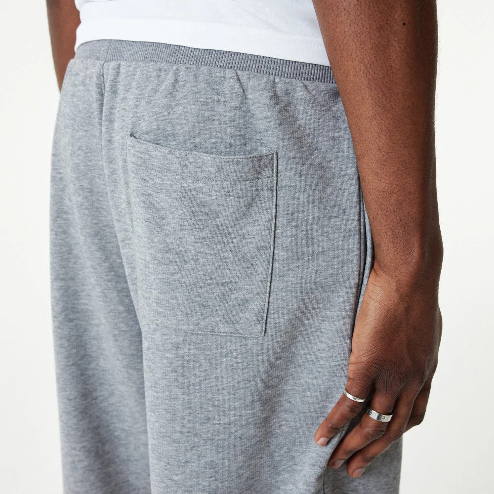New Era Essential Grey Shorts, side view displaying the light grey fabric with an elastic waistband, a patch pocket placed on the right side, and a close-up of the model's hand resting beside the pocket.