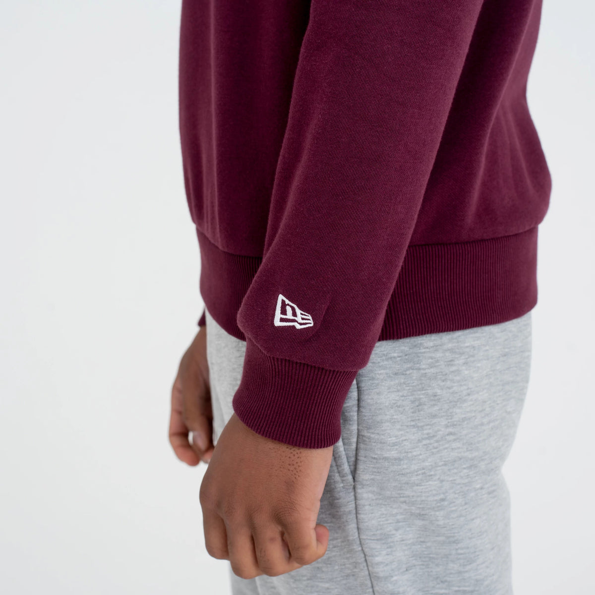 New York Yankees MLB Regular Dark Purple Crew Neck Sweatshirt, side view on a model showing the embroidered white New Era flag logo on the dark purple sleeve above the ribbed cuff, paired with light grey trousers.