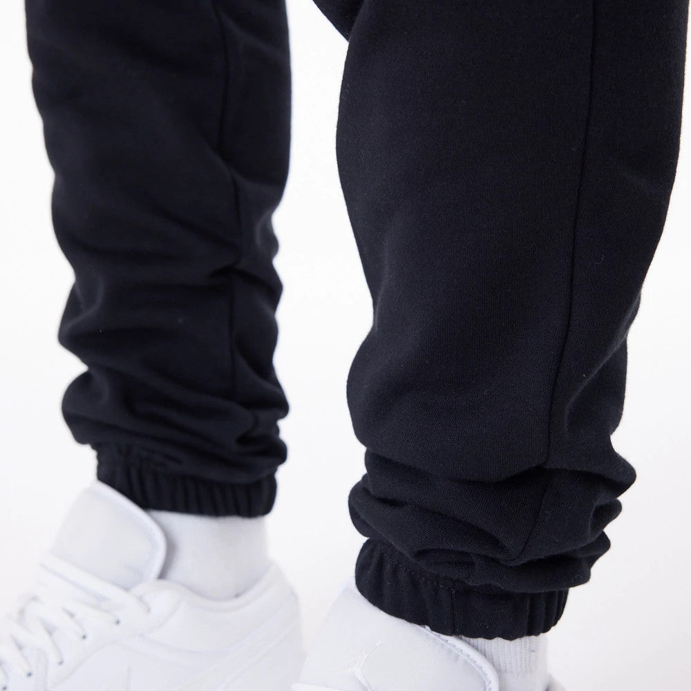 New Era Essential Black Joggers, close-up showing the elasticated cuffs gathered around the ankles and paired with white trainers, highlighting the smooth black fabric and relaxed fit.