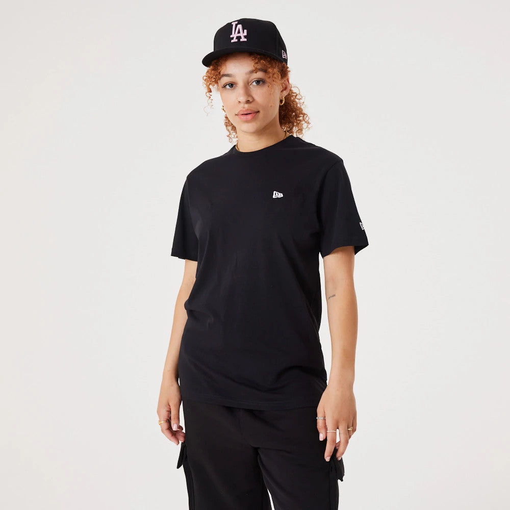 New Era Essential Black T-Shirt, on-model view showing a relaxed black tee with a raised New Era logo on the chest, paired with a black cap featuring a white LA logo, worn by a person with curly hair.