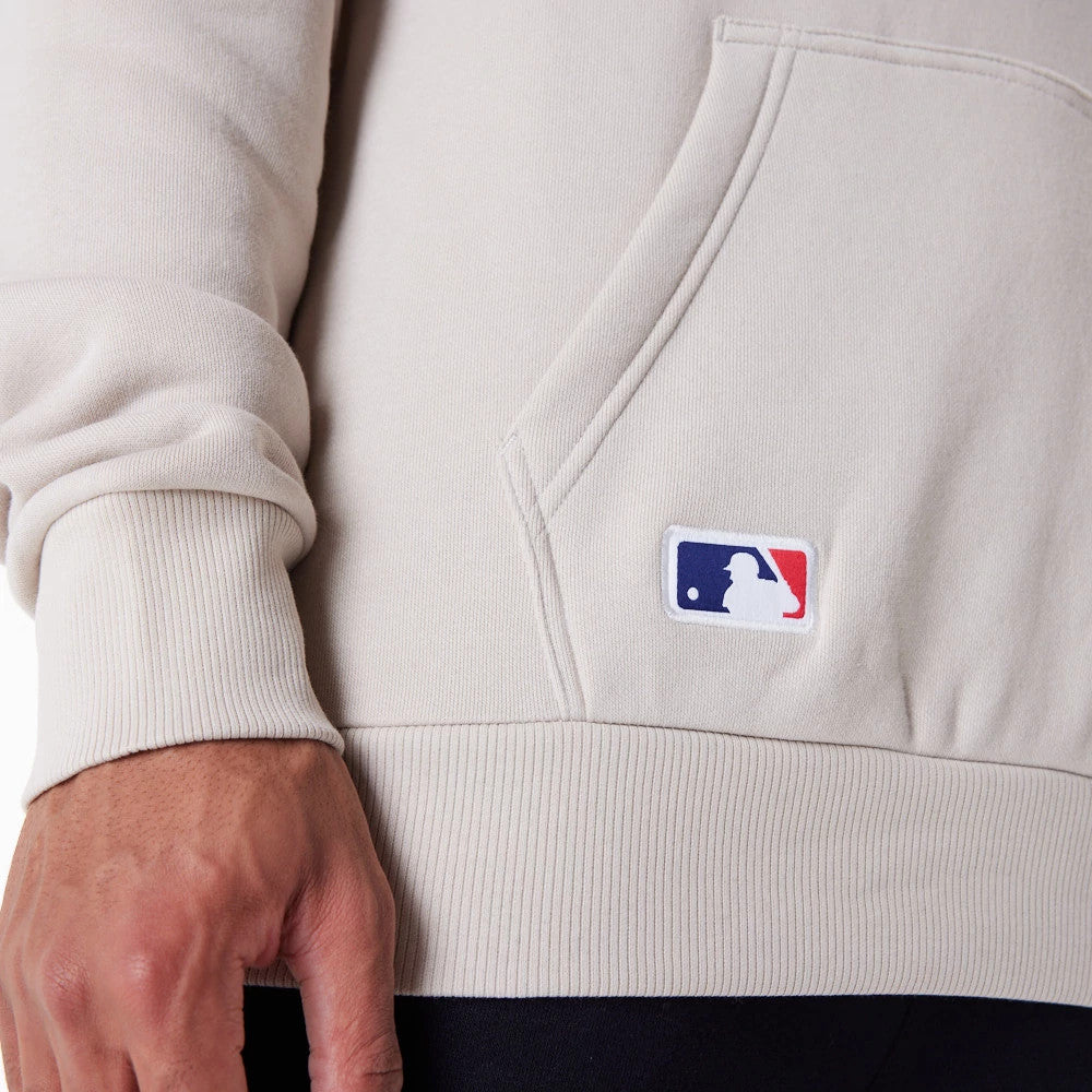 New York Yankees MLB Regular Light Beige Pullover Hoodie, side view showing a close-up of the ribbed hem and cuff, a pouch pocket and an embroidered MLB logo patch in white, red, and blue near the pocket opening.