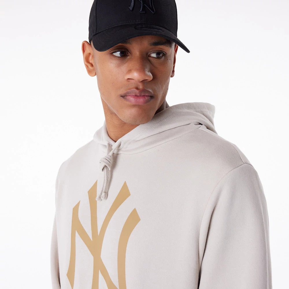 New York Yankees MLB Regular Light Beige Pullover Hoodie, front view showing a large beige Yankees logo printed on the chest, a drawstring hood, and worn with a black cap featuring a raised logo on the front.