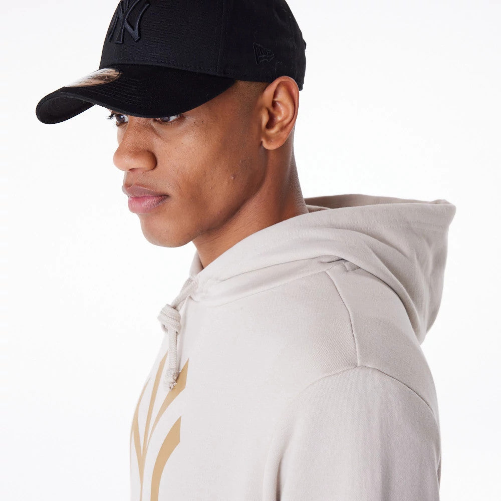 New York Yankees MLB Regular Light Beige Pullover Hoodie, on-model view showing the light beige colour with a gold New York Yankees logo on the chest, a hood with drawstrings, and a black cap with a raised New Era logo worn on the model.