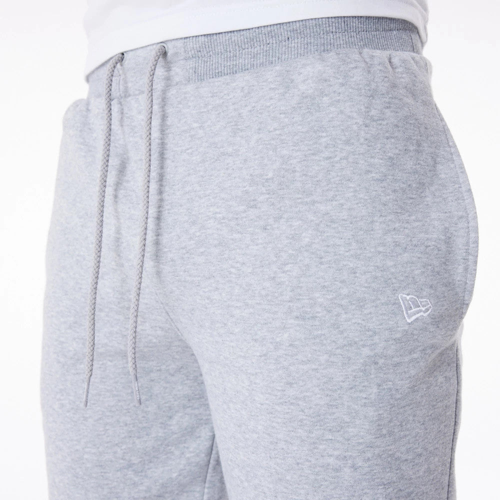 New Era Essential Grey Joggers, side view with a focus on the embroidered New Era flag logo on the left hip, featuring a ribbed waistband with grey drawstrings and a clean silhouette on a model wearing a white top.