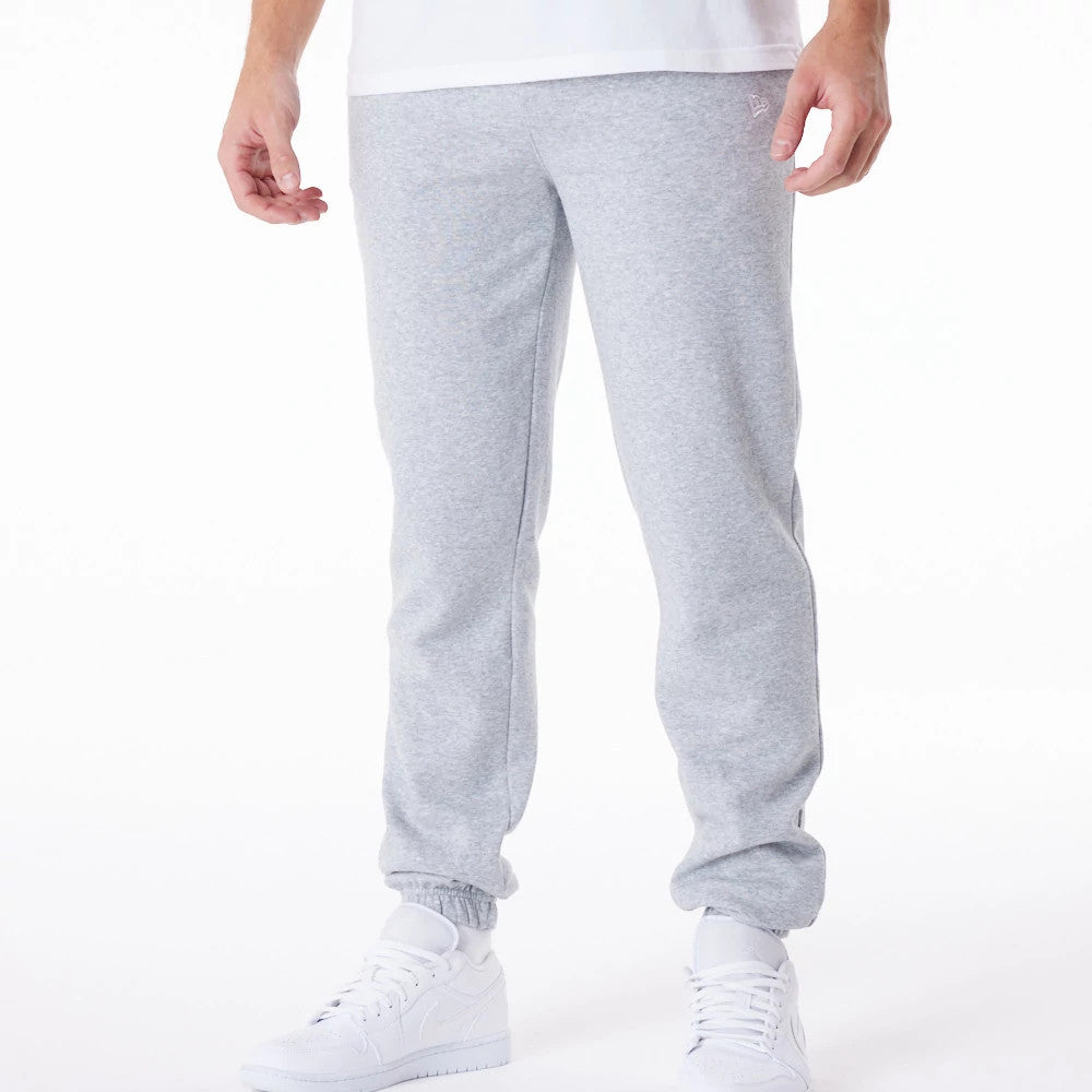 New Era Essential Grey Joggers, front view on a model wearing white trainers and a white T-shirt, showing the subtle New Era flag logo embroidered on the upper left thigh and elasticated cuffs at the ankles.