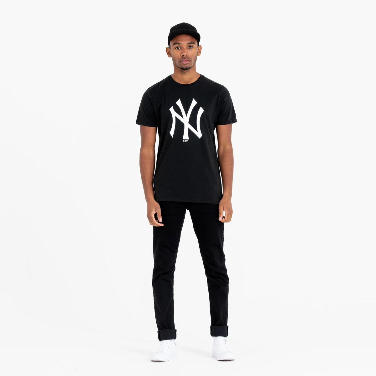 New York Yankees MLB Regular Black T-Shirt, on-model front view showing the bold white NY logo printed large on the chest of the black T-shirt, paired with black jeans and a black cap.