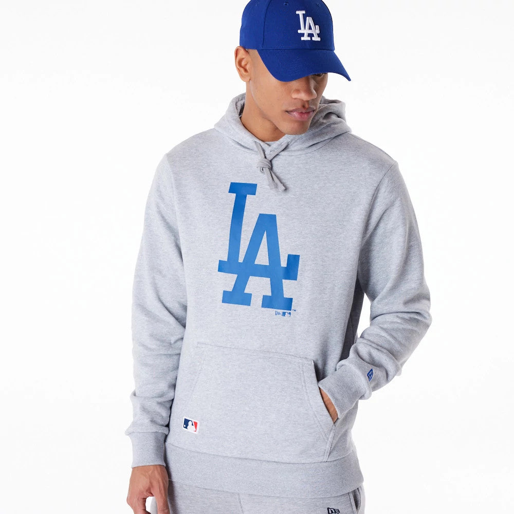 LA Dodgers MLB Regular Grey Pullover Hoodie, front view showing a large blue LA logo across the chest, a kangaroo pocket below, a debossed MLB logo near the pocket, and a blue New Era logo on a cap worn by the model.