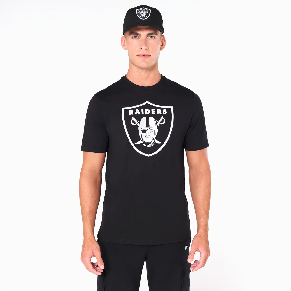 Las Vegas Raiders NFL Black T-Shirt, on-model view showing a black T-shirt with a large white Raiders logo on the chest, paired with a black cap featuring a raised Raiders logo on the front above the peak.