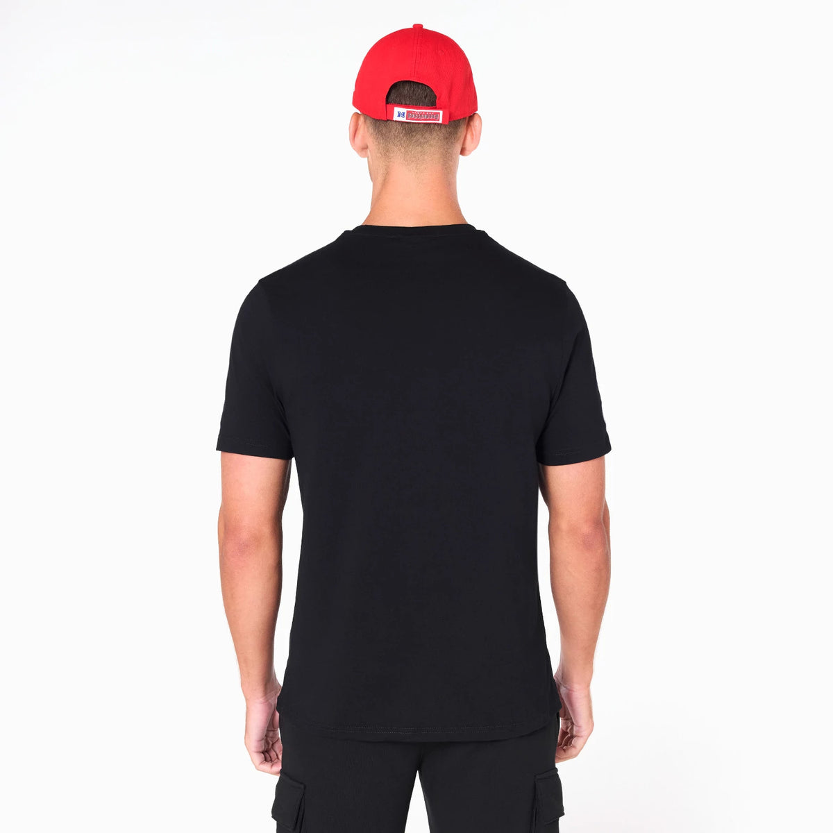Tampa Bay Buccaneers NFL Black T-Shirt, rear view showing the plain black back of the shirt worn by a person, with the short sleeves and crew neck visible, paired with a red cap displaying a logo above its closure.