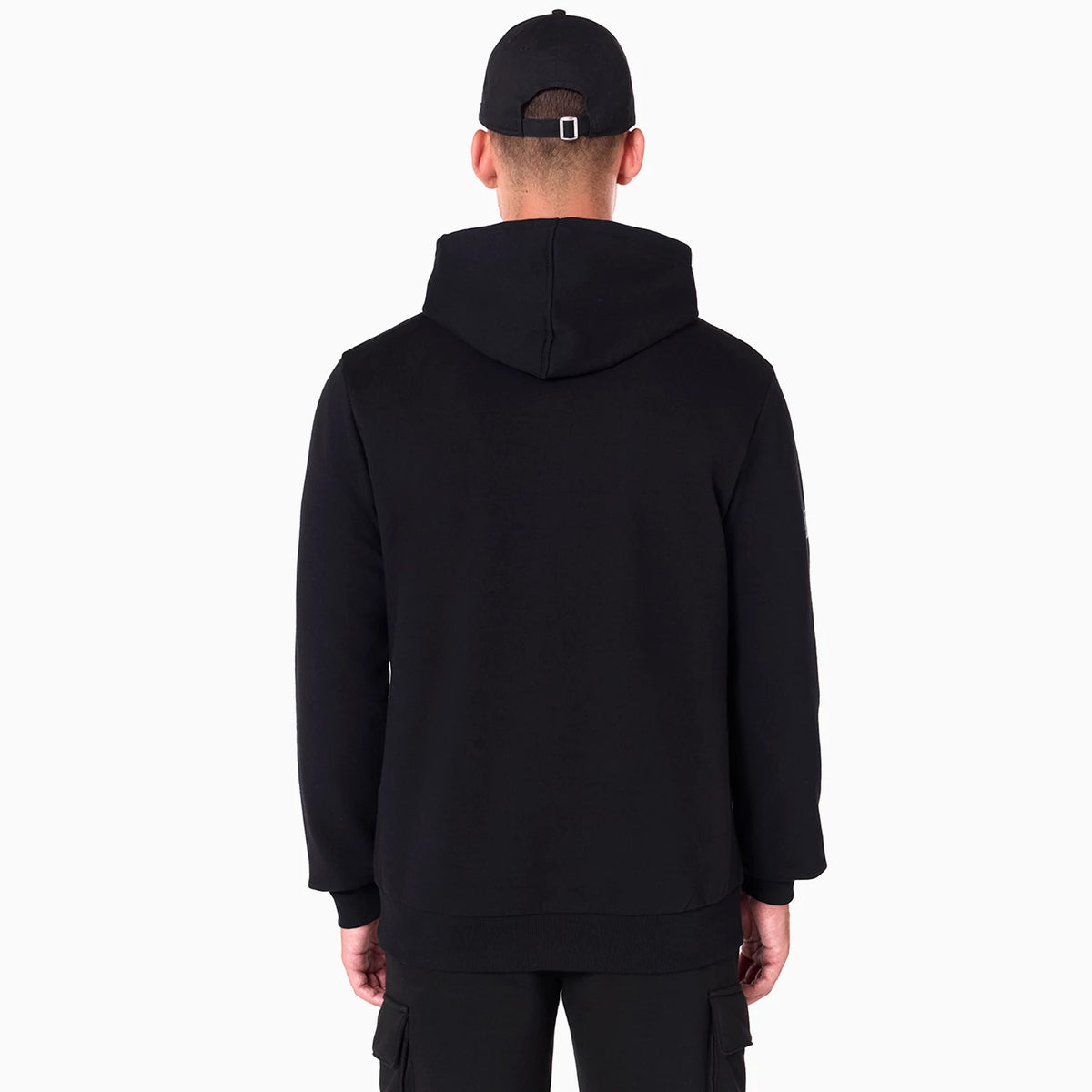 NFL Shield Logo NFL Black Pullover Hoodie, rear view showing the plain black hoodie with a relaxed fit and the hood resting flat on the back, worn by a person with a black New Era cap featuring a debossed logo and eyelets.