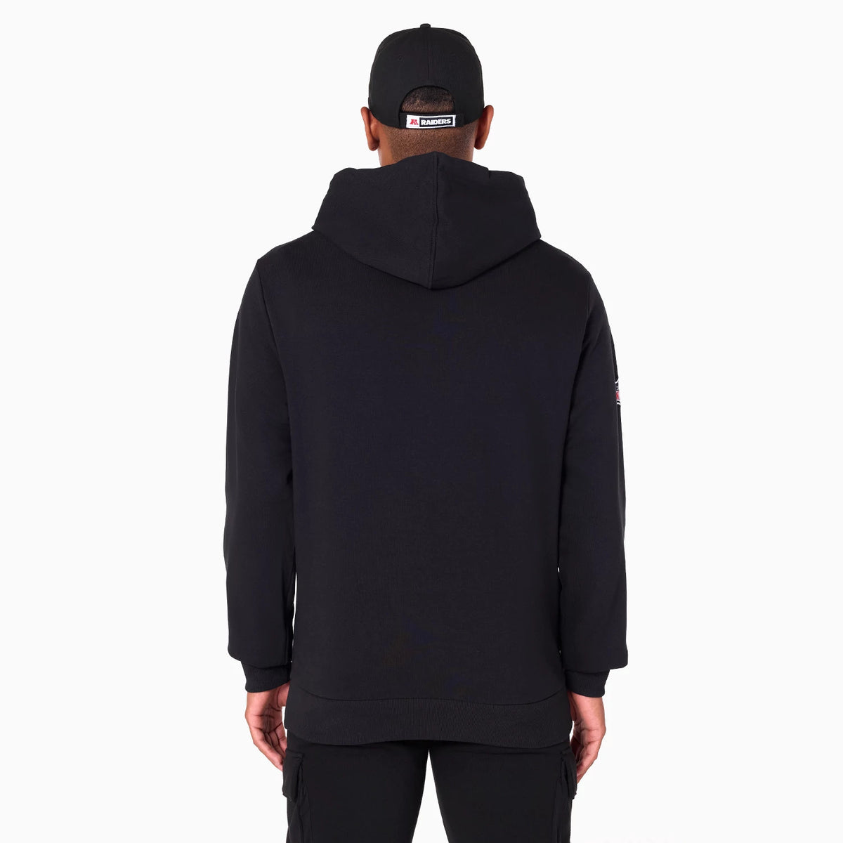Las Vegas Raiders NFL Black Pullover Hoodie, rear view showing the plain black hoodie with its large hood draped over the shoulders, long sleeves, and a small logo patch on the upper left sleeve, worn by a person facing away.