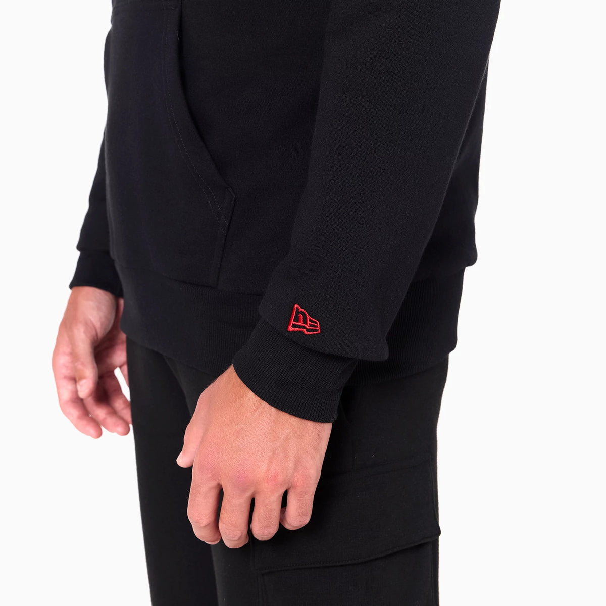 Tampa Bay Buccaneers NFL Black Pullover Hoodie, side view showing a close-up of the lower half with a red embroidered New Era logo on the cuff and the pocket visible on the front against the black fabric.