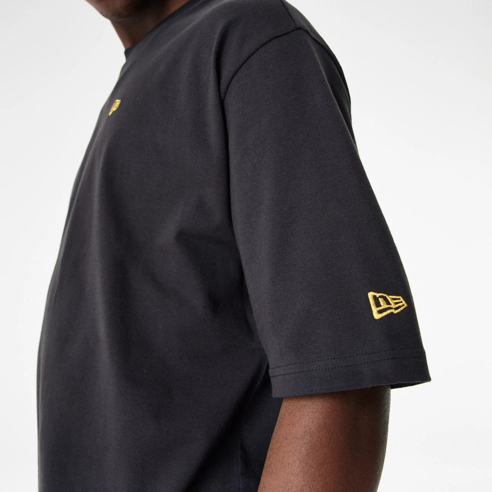 New Era Lifestyle 59FIFTY Black Oversized T-Shirt, side view showing a loose fit with the short sleeve featuring a raised gold New Era logo near the hem and a small gold logo on the chest.