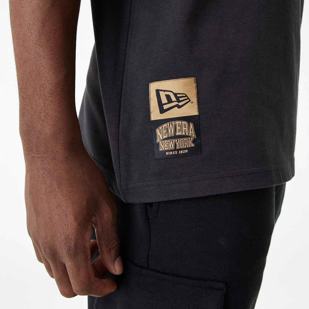 New Era Lifestyle 59FIFTY Black Oversized T-Shirt, side view showing the black fabric with a beige patch on the lower side, featuring an embossed New Era logo above the text "New Era New York Since 1920".