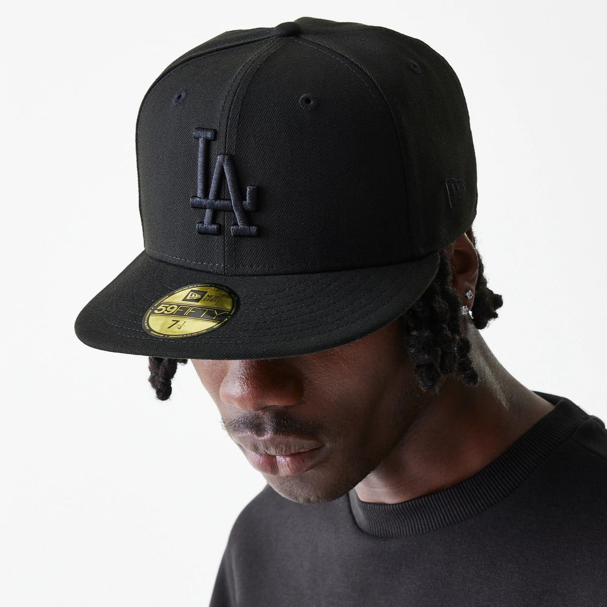 LA Dodgers League Essential Black New Era 59FIFTY Fitted Cap, on-model view showing a raised black LA logo on the front panel, black structured crown, pre-curved black visor and gold 59FIFTY size sticker on top.