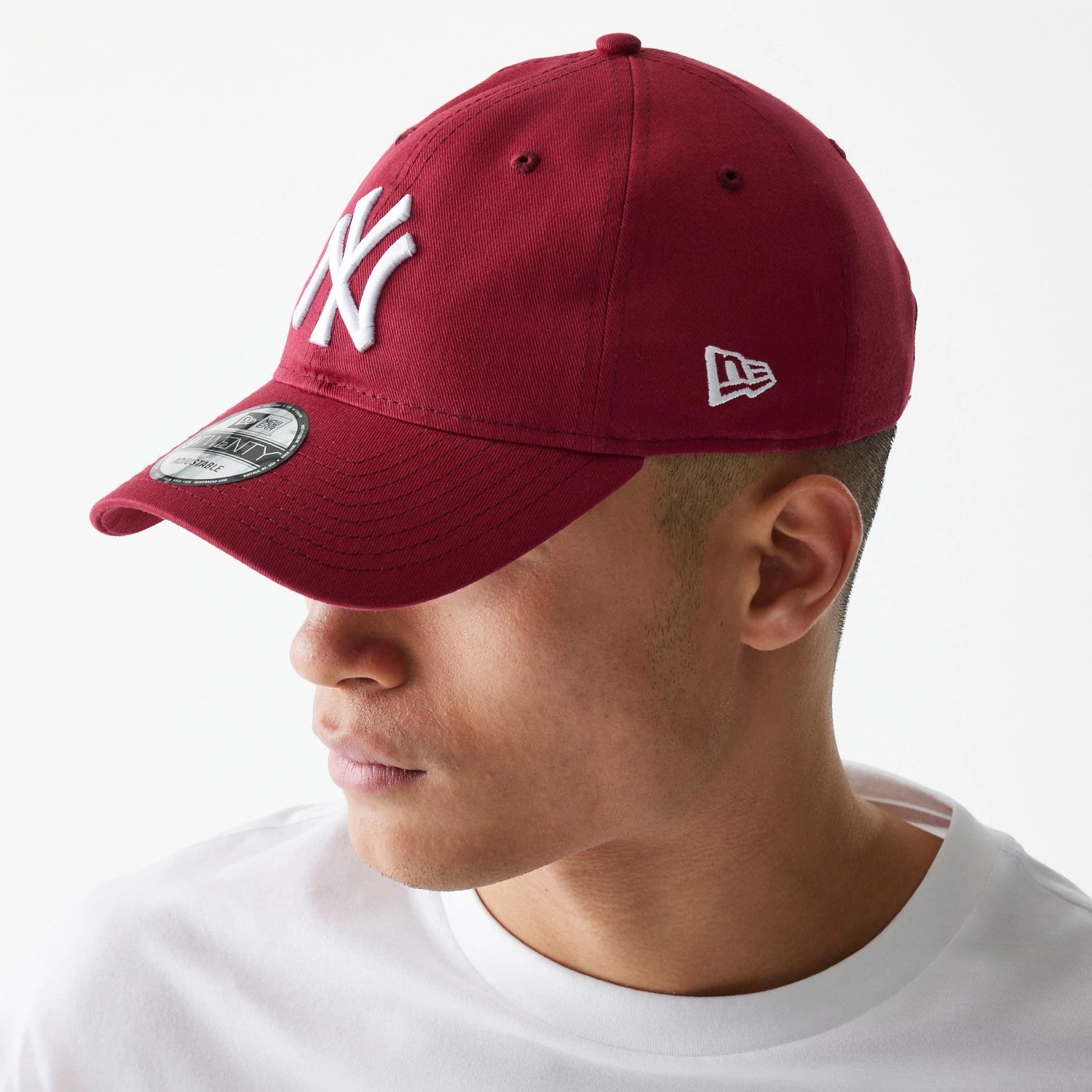 New York Yankees League Essential Dark Red New Era 9TWENTY Adjustable Cap, three-quarter view on a model wearing a white T-shirt, showing the raised white Yankees logo on the front panel and New Era flag logo on the left side.