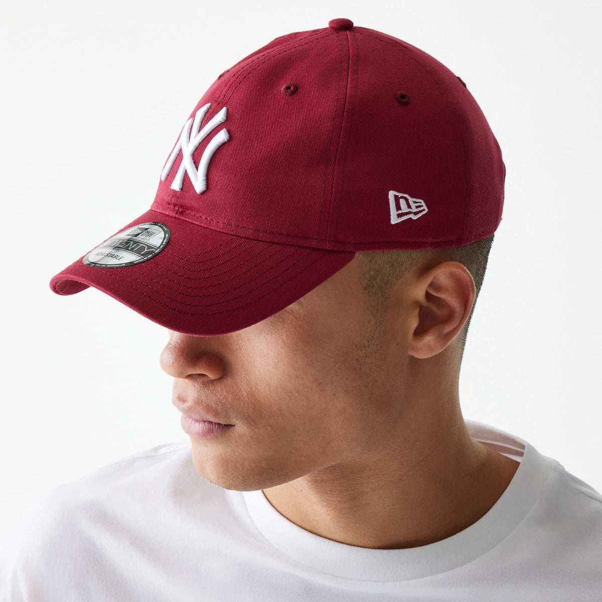New York Yankees League Essential Dark Red New Era 9TWENTY Adjustable Cap, three-quarter view on a model wearing a white T-shirt, showing the raised white Yankees logo on the front panel and New Era flag logo on the left side.